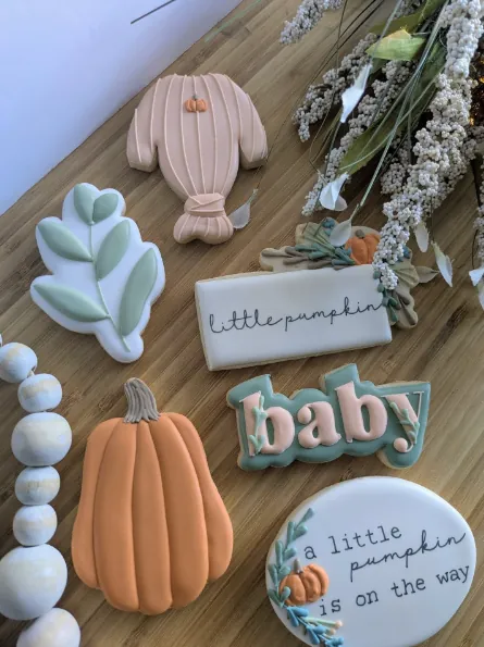 Neutral baby shower cookies with pumpkins, a romper and baby lettering